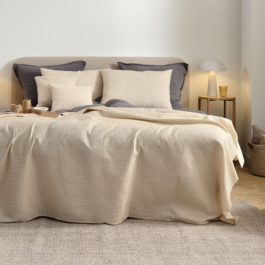 Sengeteppe, ryggputer og puter i varme beige fargetoner på en dobbeltseng på soverommet