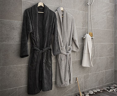 To grå badekåper som henger på et bad