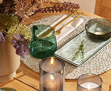 Detaljbilde av bord med krus, spisebrikke, lys, skål og en krukke med kunstige blomster