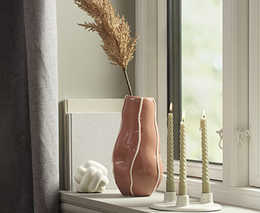 Ferskenfarget, dekorativ og skulpturellt utformet vase i en vinduskarm