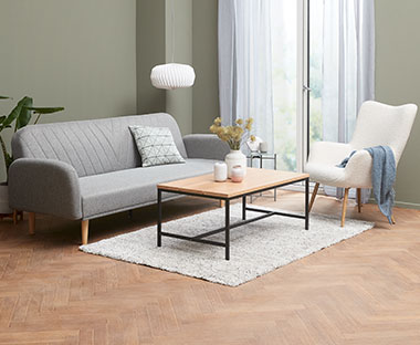 Sovesofa i lys grå tekstil og et sofabord med sorte ben i en stue