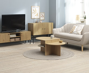 Stue innredet med lys sofa og naturfargede møbler som stuebord, skjenk og TV-bord