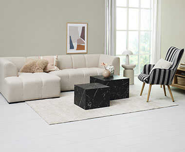 En stue innredet med trendy møbler som en offwhite sofa, sofabord i sort marmor look med stripete lenestol