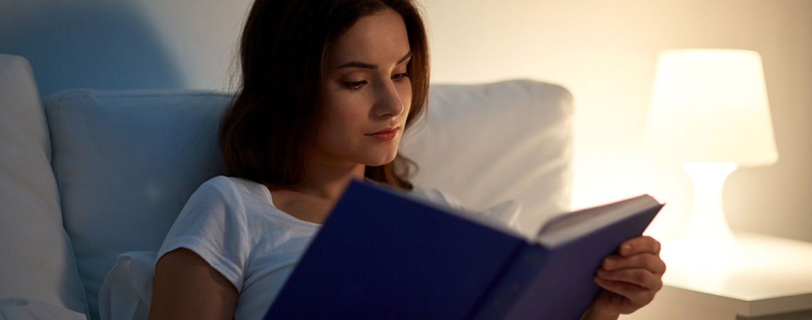 Kvinne som leser bok i sengen