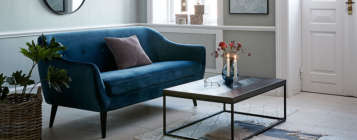 Stue med en blå velour sofa og et sofabord med tente stearinlys