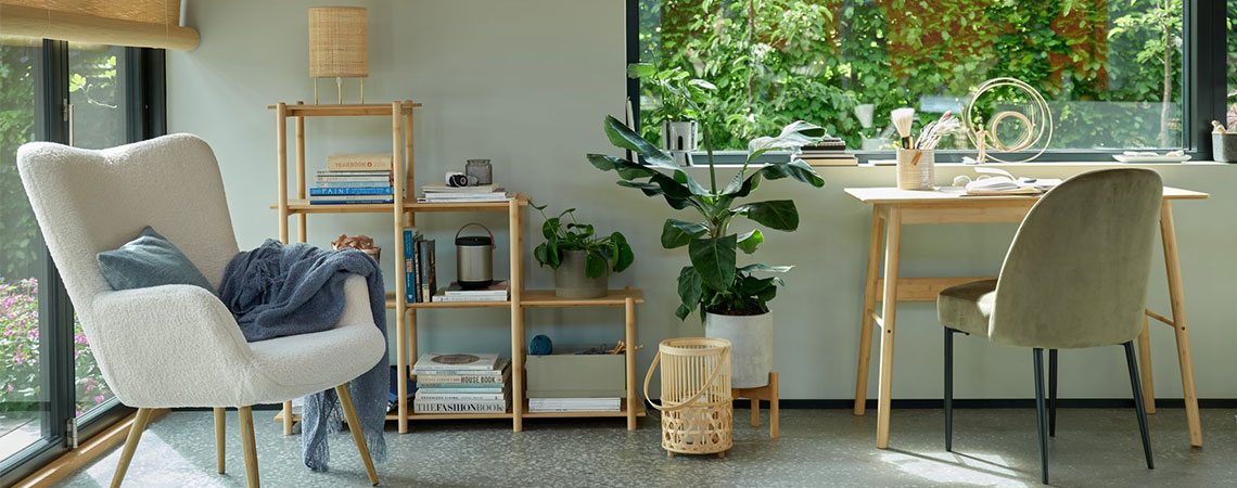 Grå lenestol ved et vindu og en reol i bambus bakgrunnen. Bambuslykt på gulvet ved siden av et bambusbord og en olivengrønn spisestol