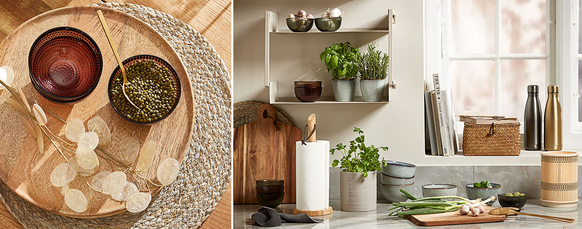 Glasskåler på en flettet spisebrikke og steintøykrus med friske urter på en vegghylle på et kjøkken