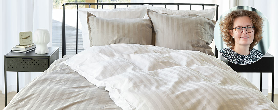 Soverom med seng, dyner og puter, dekket av stripete sengetøy og bilde av Berit Christiansen