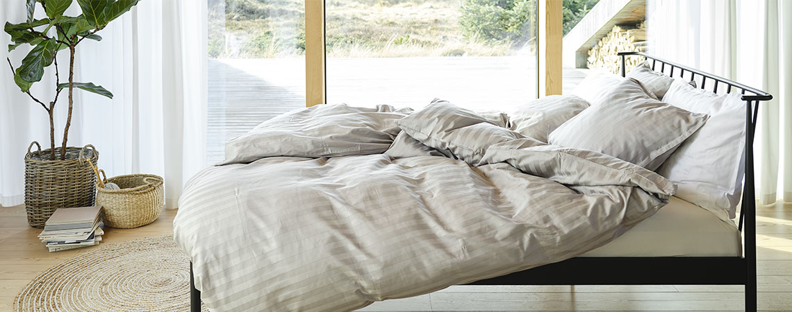 Soverom med svart metallseng, dyner og puter, dekket av stripet sengetøy i lysegrått og hvitt 