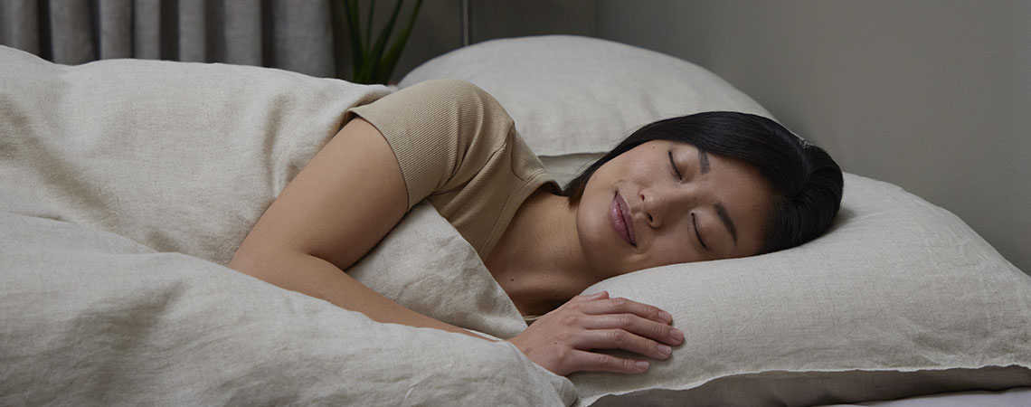 Kvinne som sover på siden i sengen med pute og dyne i beige sengetøy