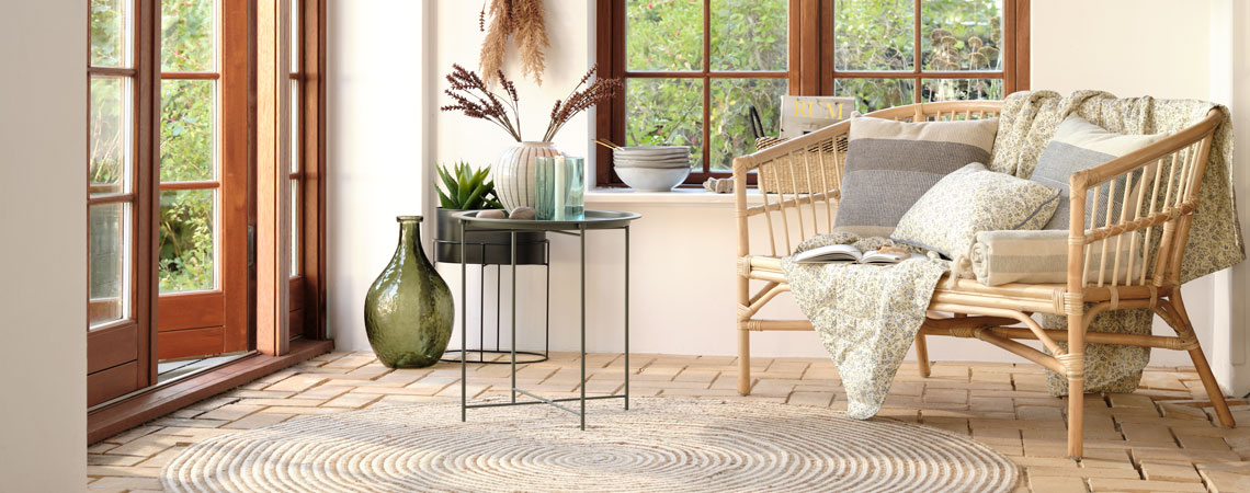 Grønn gulvvase, svart sidebord og sofa med vattert teppe og pyntepute med blomstermønster