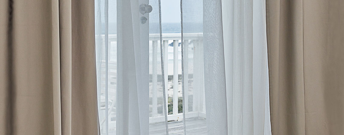 Utsikt mot en balkong gjennom en åpen dør med blafrende gardiner
