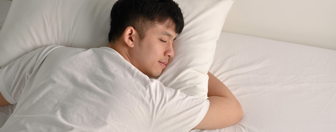 Mann som sover fredelig i sengen med hvit pute og hvit overmadrass