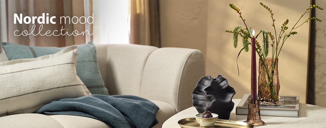 En stue med sofa og sofabord med glassvase og lysestake 