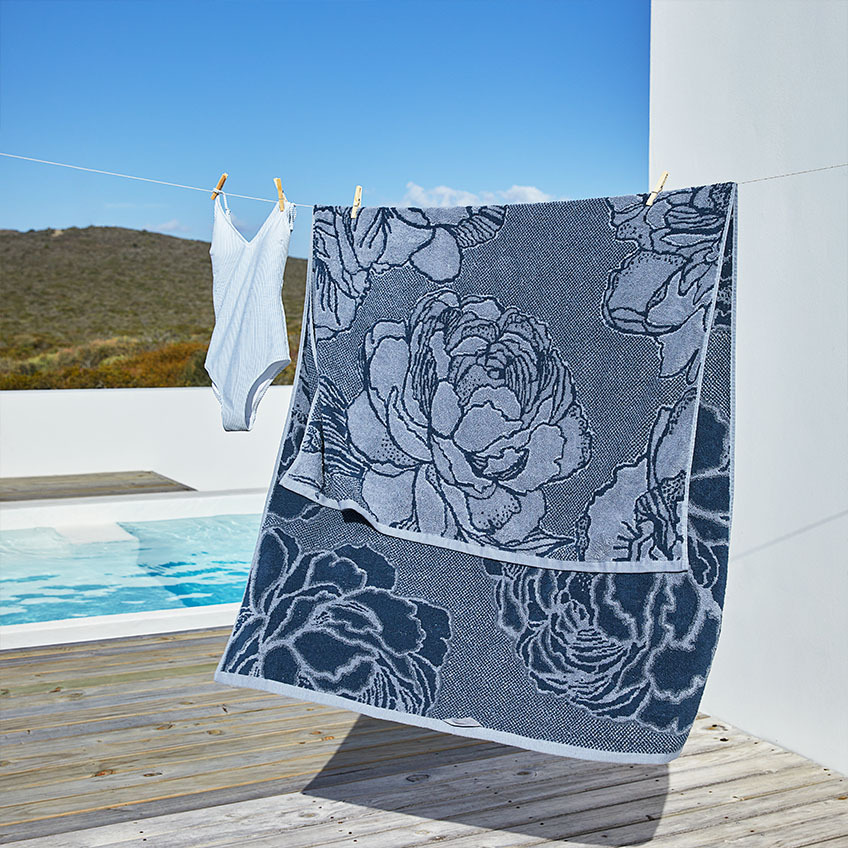 Stort blått badehåndkle med blomstermønster på tørkesnor 