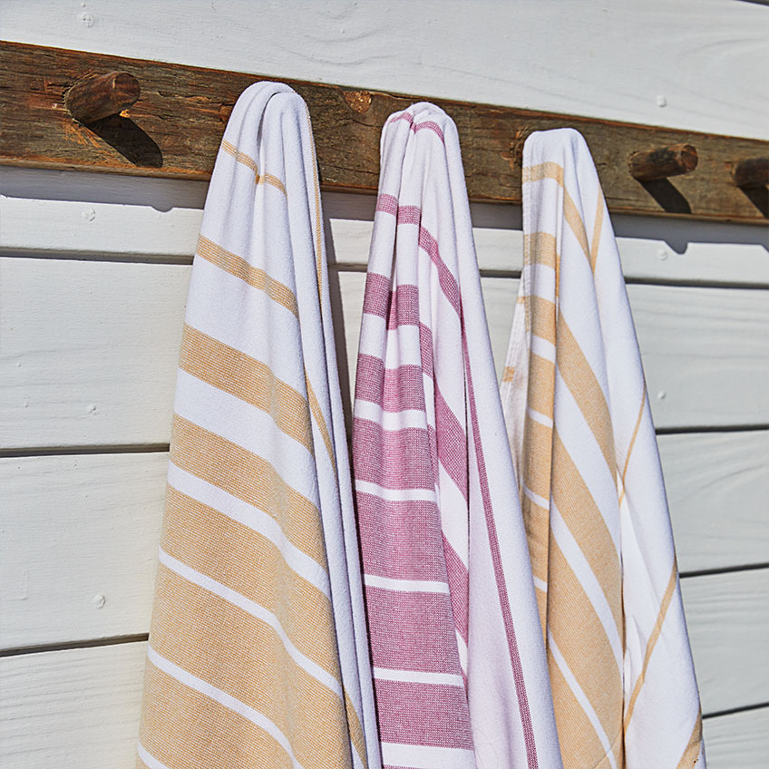 Stripete badehåndklær i hvitt, oransje og rosa henger på trevegg 