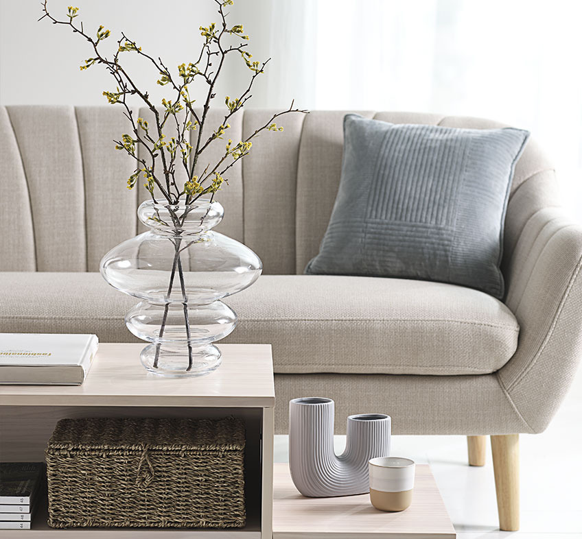 SYLVESTER glassvase, TORMUND vase, og FREDERIK krus Lys stue med lekne vaser på salongbord og en beige sofa i bakgrunnen