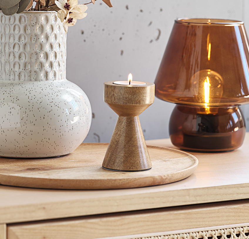 INGBERT vase, JOHAN telysholder og HOLGER batterilampe En beige vase, telysholder i mangotre og en brun batterilampe i glass på en skjenk