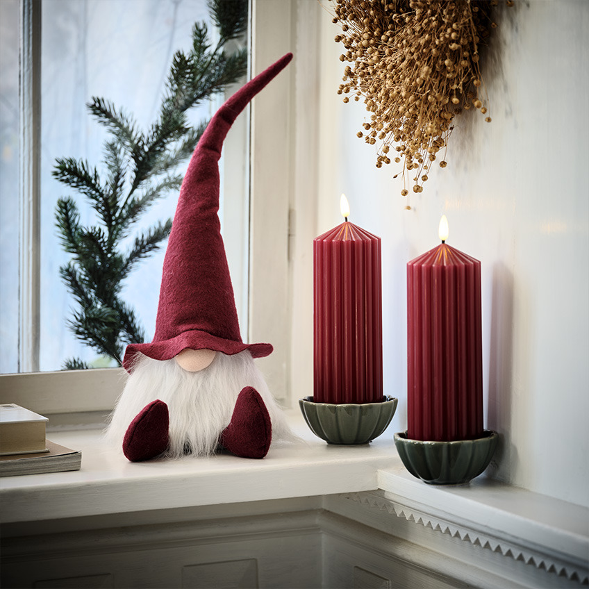 Skandinavisk julenisse i vinduskarmen ved siden av store, røde lys   
