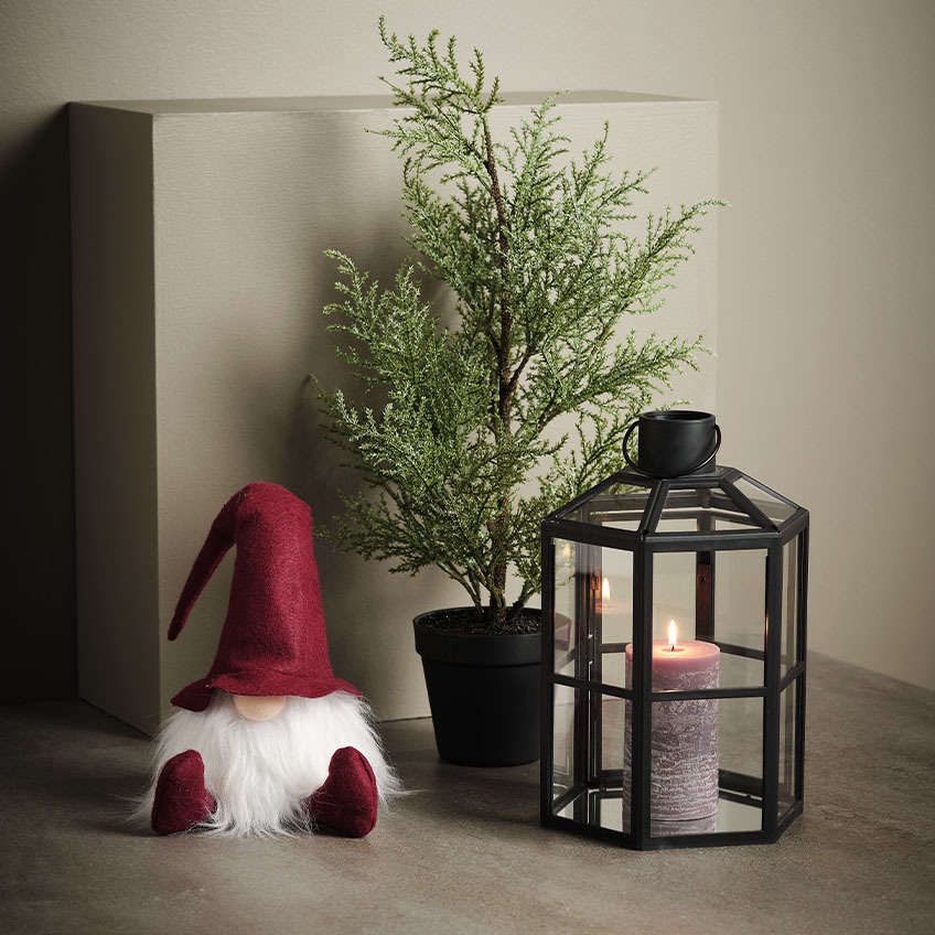 Skandinavisk julenisse ved siden av kunstig plante og lykt  