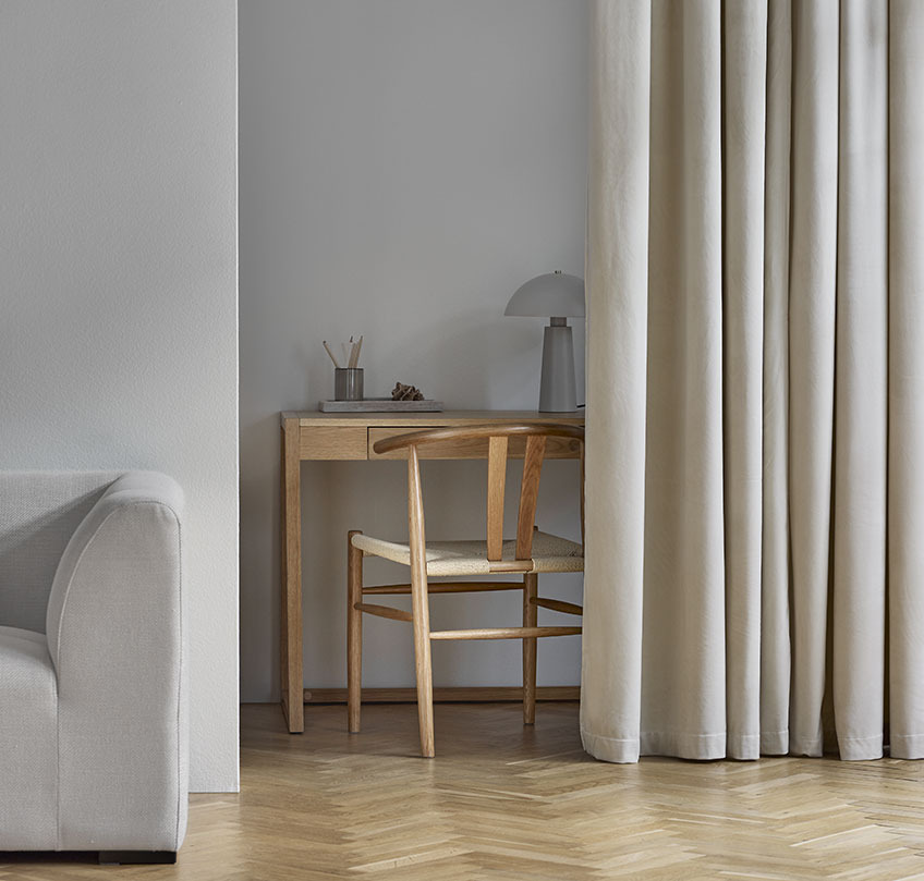 Beige gardiner som skiller et hjemmekontor med skrivebord og stol fra en stue