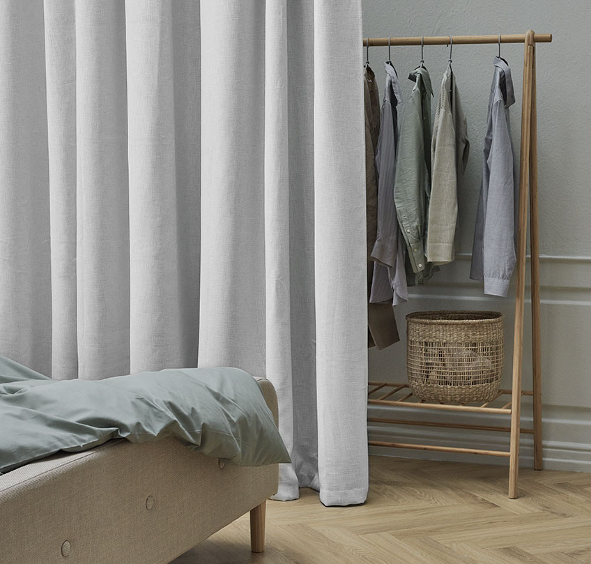 Beige gardin foran et garderobestativ skiller et soveområde fra et garderobeområde