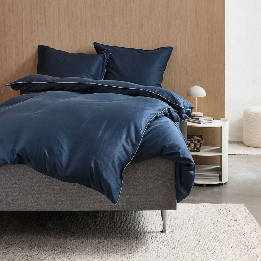 Satengsengesett i mørkeblått med lyseblå kantbånd på sengen på et soverom