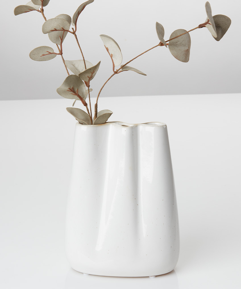 Hvit vase med organiske linjer og bølgete kanter og kunstig kvist
