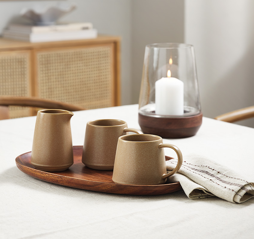 Krus og melkekrukke i brunt stentøy på et spisebord med servietter og duk