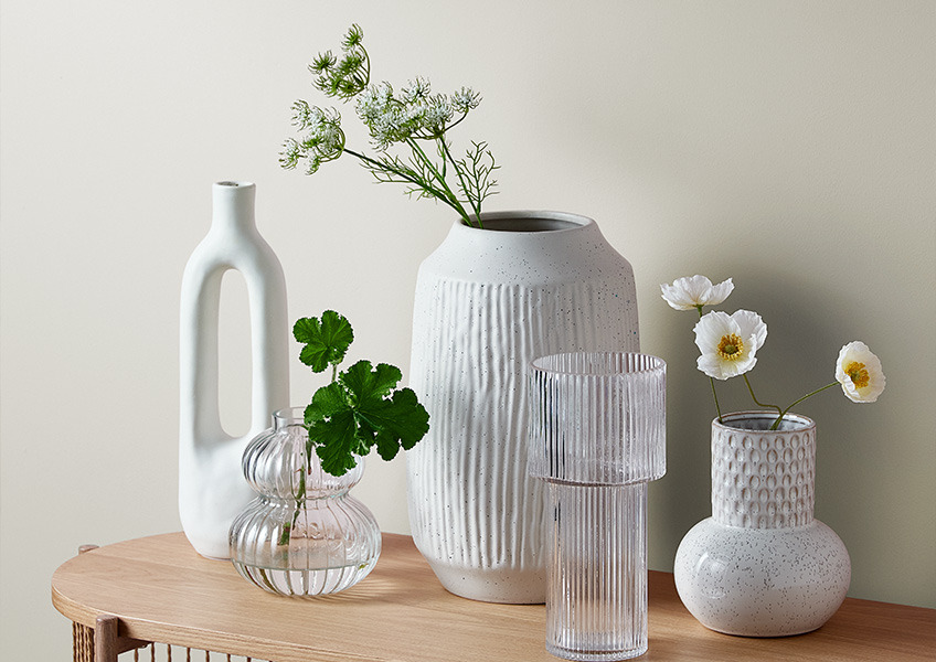 Ulike vaser med kunstige og ekte blomster på en skjenk
