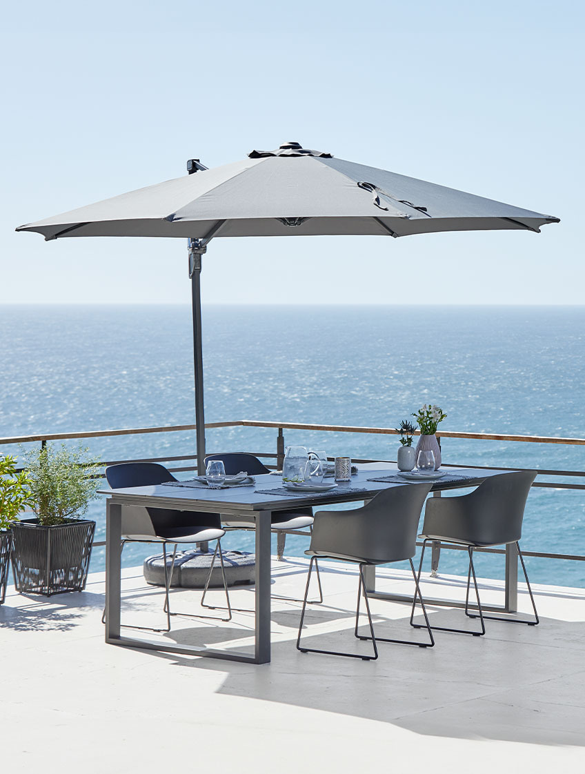 Stor hengende parasoll og hagebord med stoler på en terrasse ved havet