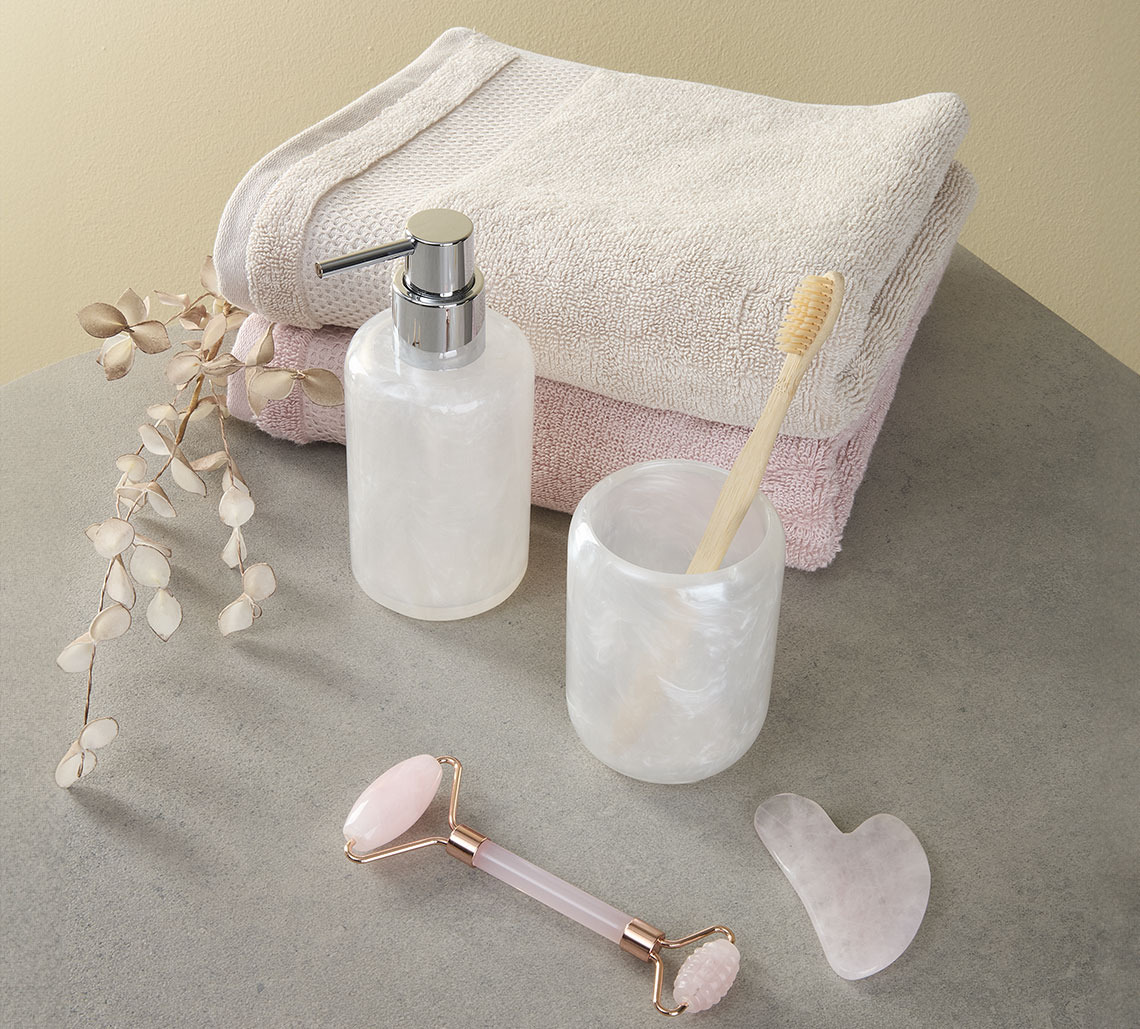 Sandfarget og rosa håndkle ved siden av tannbørsteholder, såpepumpe og ansiktsrulle 