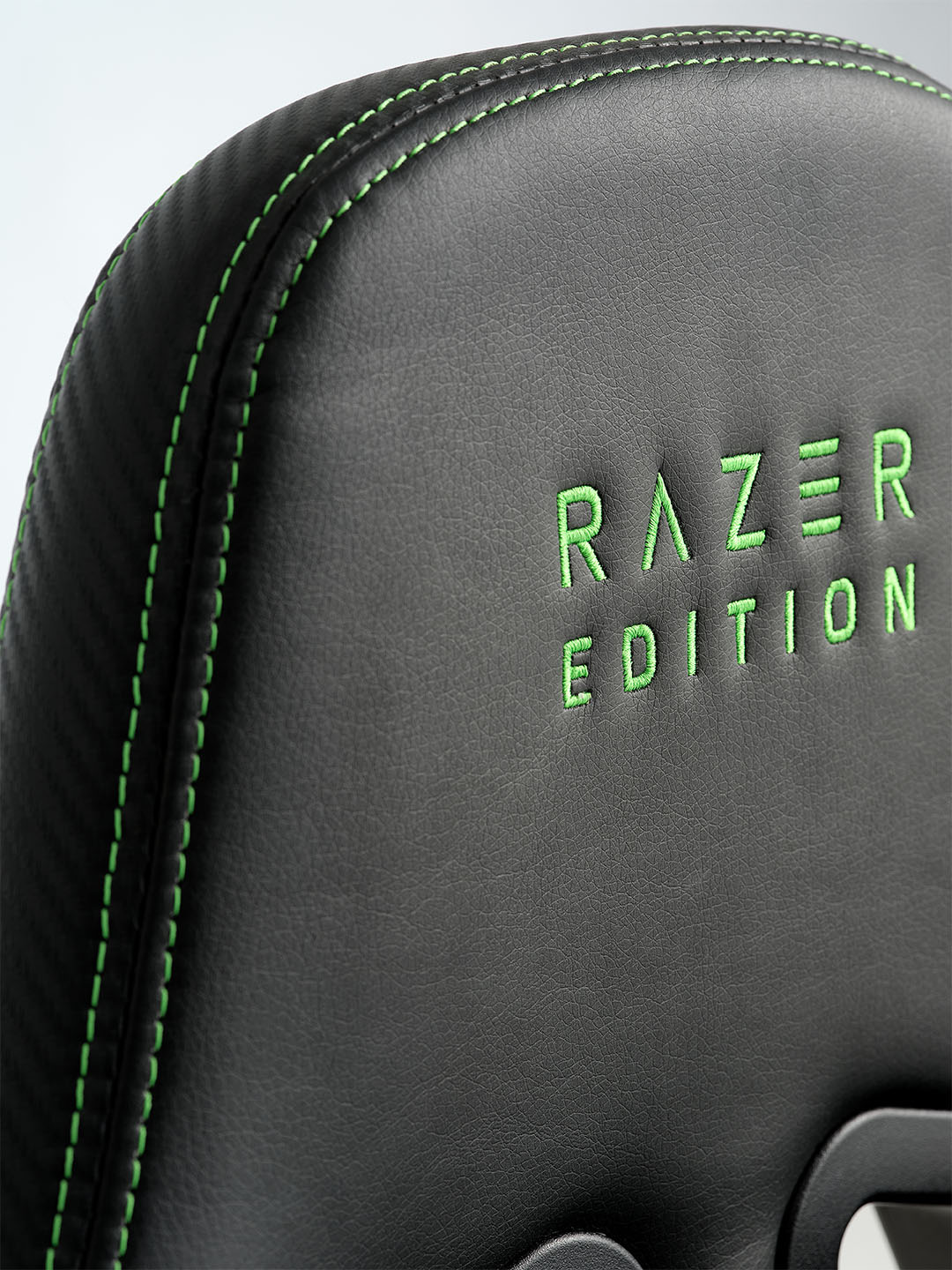 TYPE Z – RAZER EDITION™ BY LEGEND gamningstol Nærbilde av en svart razer-gamingstol med grønne sømmer, med "RAZER EDITION" brodert i grønt på ryggstøtten.