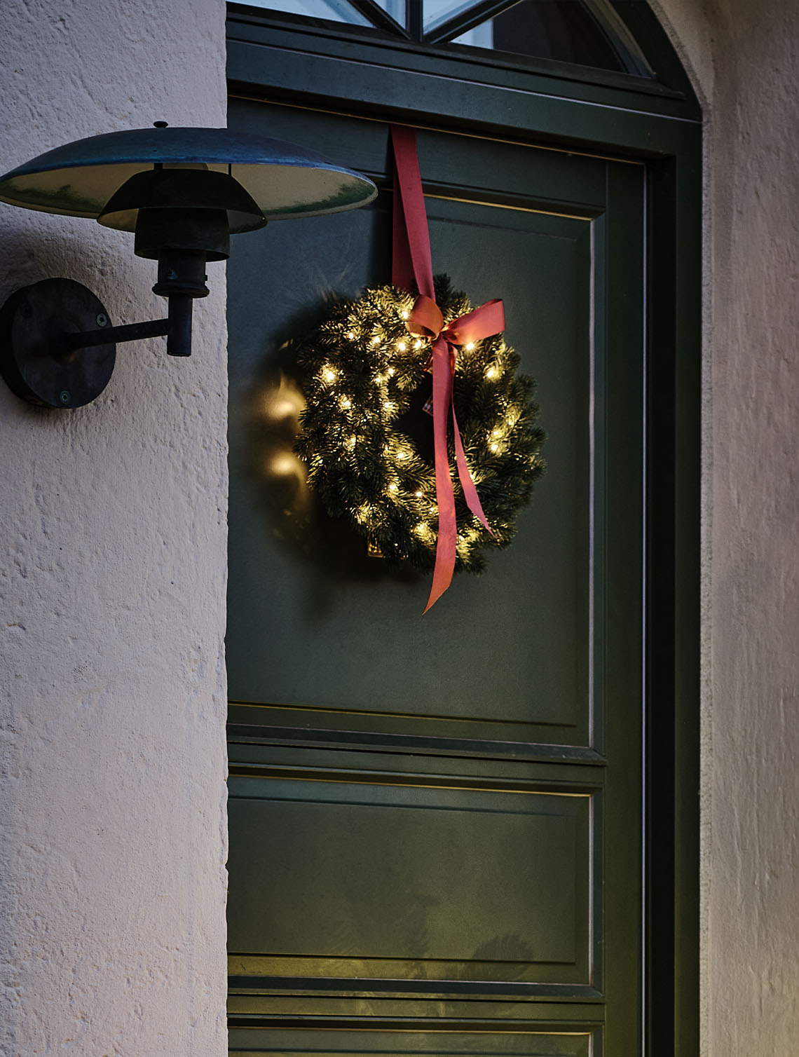 Utendørs julekrans opplyst med små lys hengt på en dør