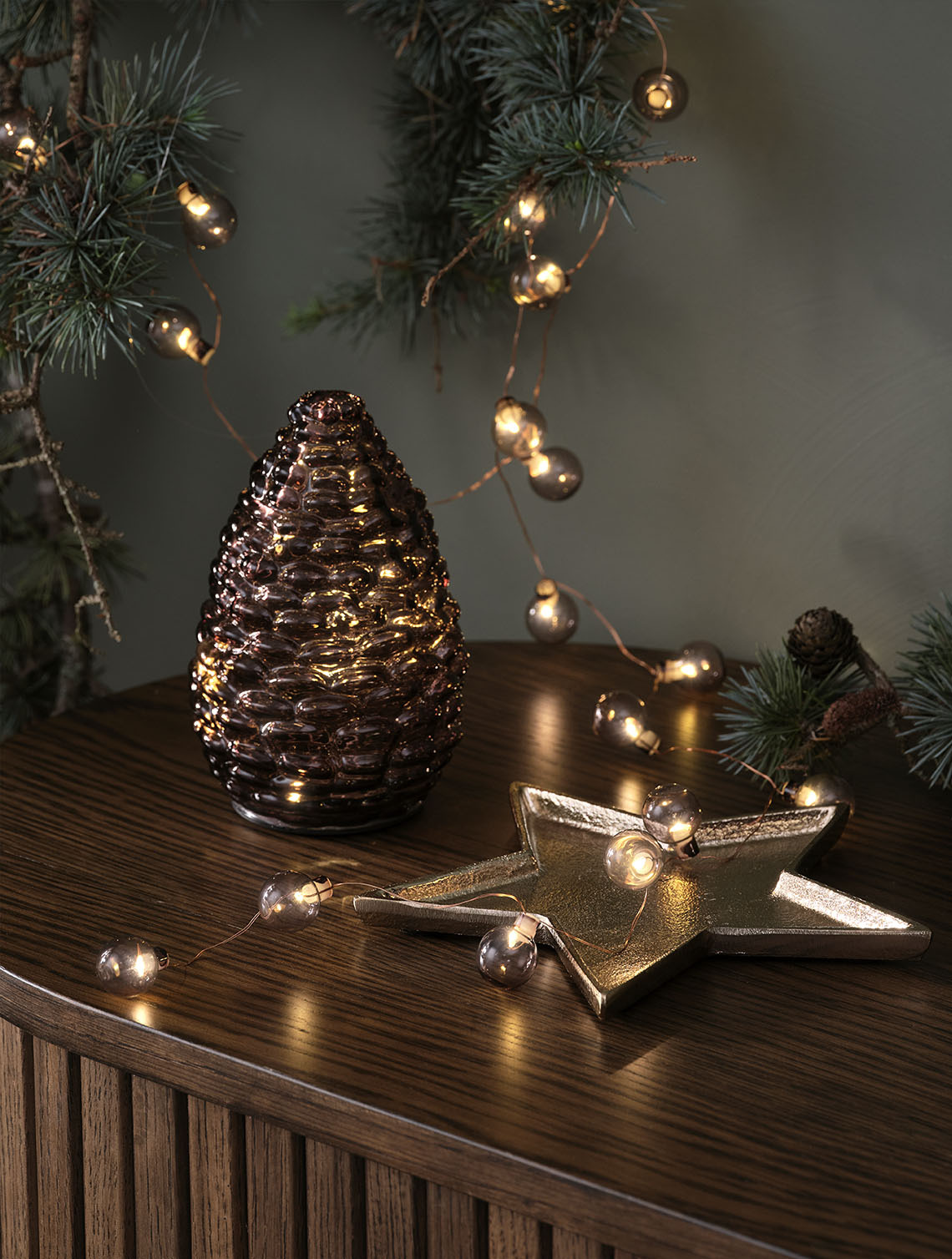 Dekorativ julebelysning som en kongle i glass og lyslenke med runde lyspærer på en skjenk