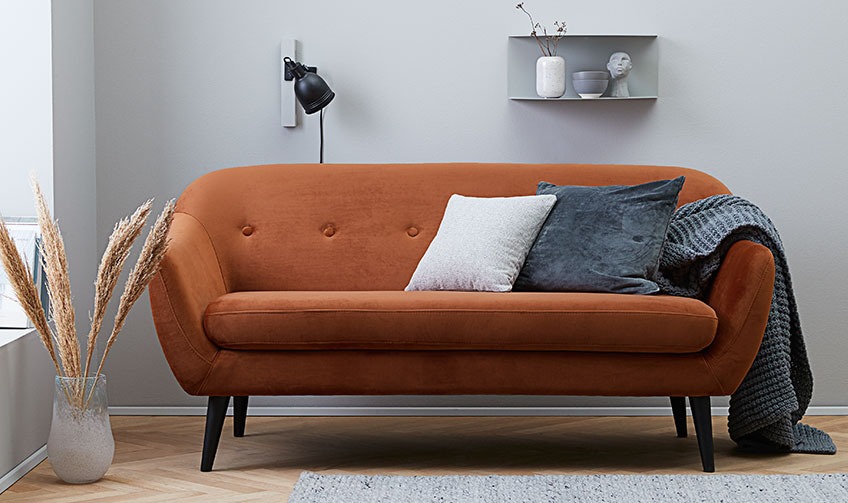 Stue med en orange sofa fylt med puter og et pledd