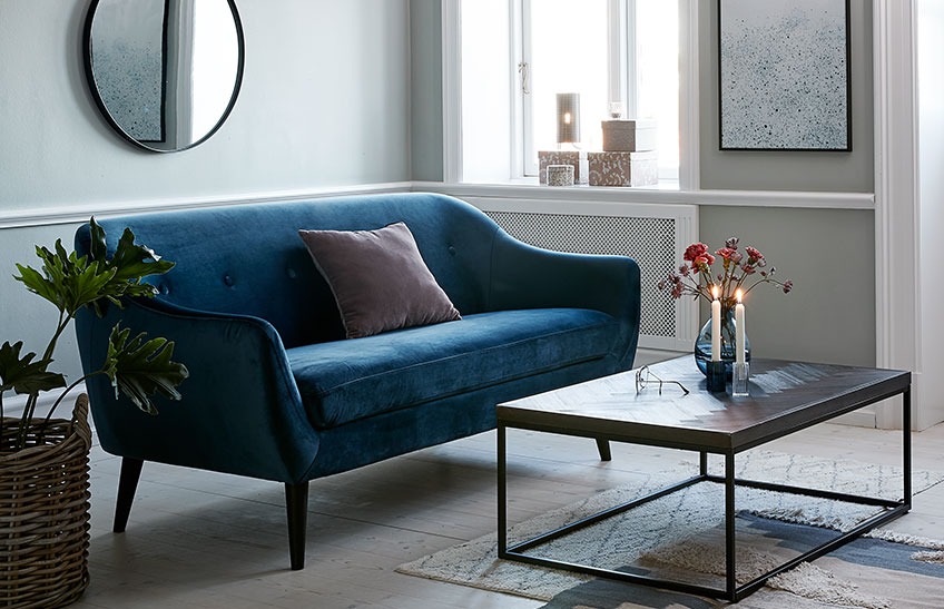 En stue med en blå fløyelssofa og et stuebord
