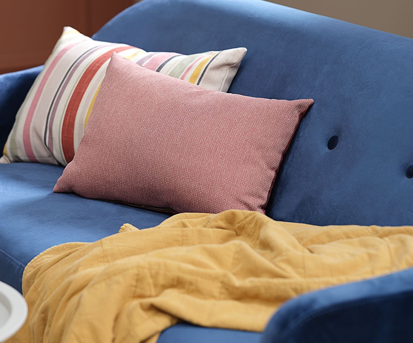 Colourful cushions and a quilted blanket in a blue sofa