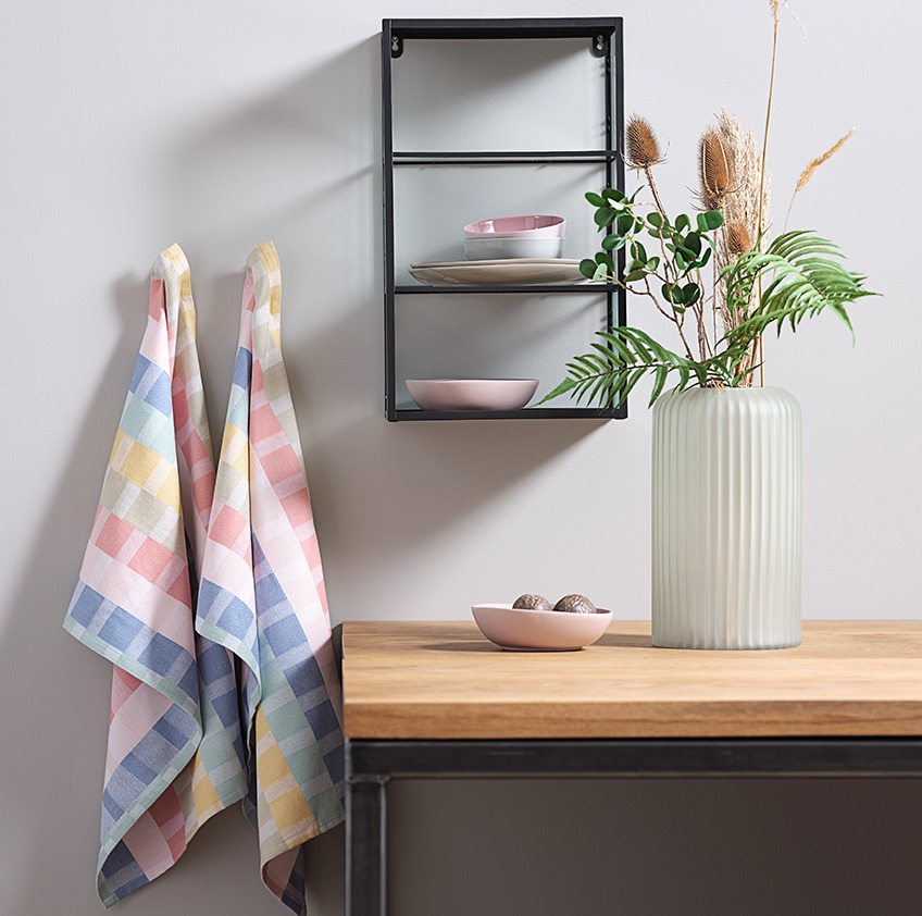 Bomulls kjøkkenhåndklær hengende ved siden av en vegghylle og en vase på et bord