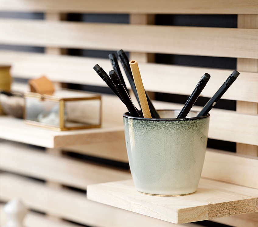 A mug with pencils on a wall shelf