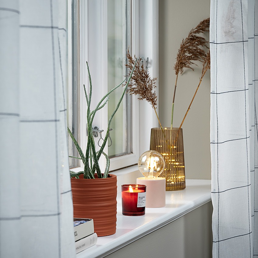 VIGRA curtains, EJLEV plant pot, JENS scented candle, ARNOLD battery lamp and ROY vase Lightweight curtains in a window with plant pot, scented candle, battery lamp and vase in the windowsill