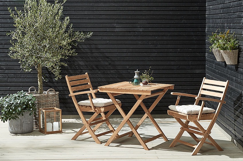A bistro set with a small table and two folding chairs in the corner on a patio