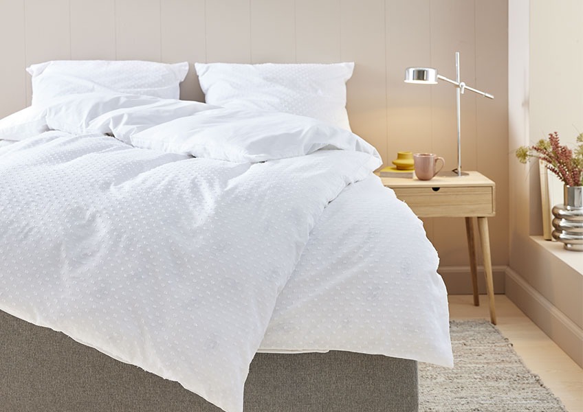 Seng med hvitt prikkete dynetrekk på et soverom med nattbord og krom bordlampe