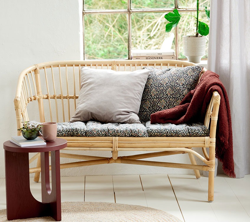 LISELEJE 2-seters sofa i rotting med TOPPKLOKKE sitteputer og pute, ROSE pledd og ARCH sidebord 2-seters sofa i rotting med sitteputer og ryggputer, burgunder pledd og et rundt sidebord