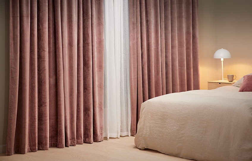 Lun atmosfære på soverommet med lystette rullegardiner og tykke pyntegardiner