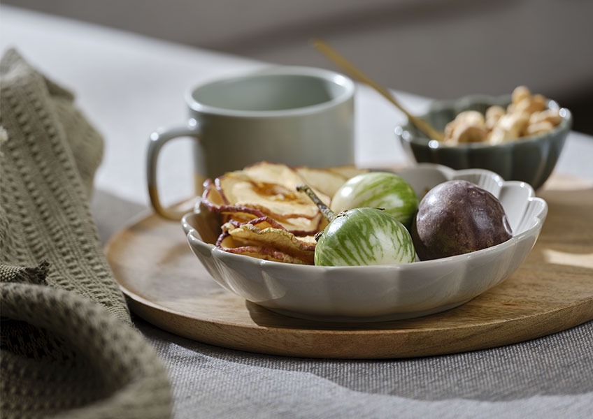 Trebrett med grå bolle fylt med frukt plassert på sofaen