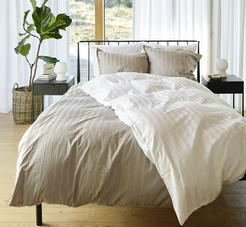 Soverom med grått og hvitt stripet sengetøy på sengen og to nattbord 