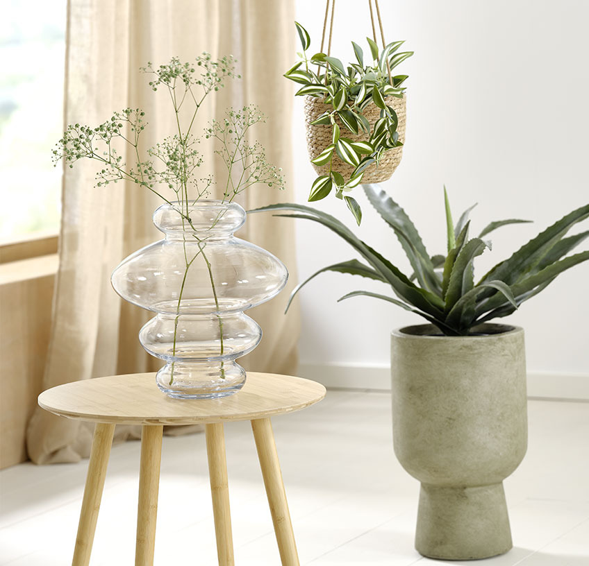 Glass vase on an end table, hanging plant pot and green plant pot with artificial plants 
