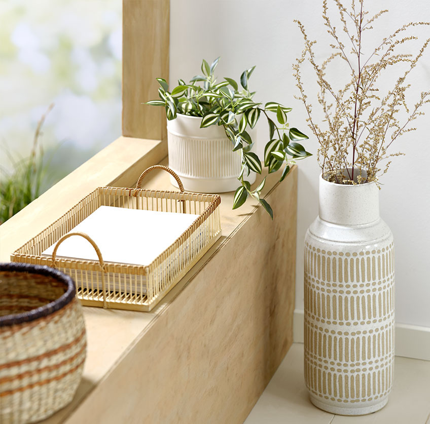 Høy vase ved siden av vinduskarmen med bambusbrett og hvit blomsterpotte med kunstig plante 