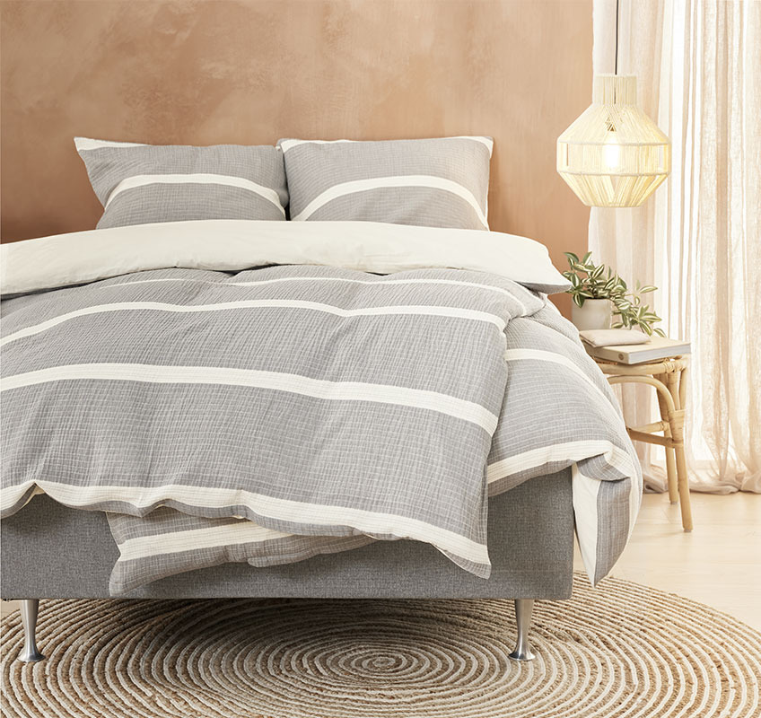 Seng med sengetøy i grå og beige farger 